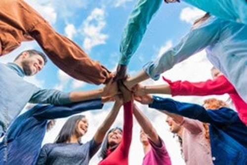 Diverse group of people standing in a circle with hands joined in the center, symbolizing teamwork, unity, and inclusive culture.