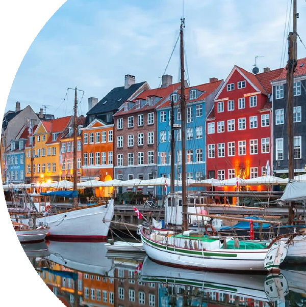 Scenic view of Nyhavn in Copenhagen, featuring colorful historic buildings along the waterfront, with sailboats docked in the canal and soft afternoon lights reflecting on the water.