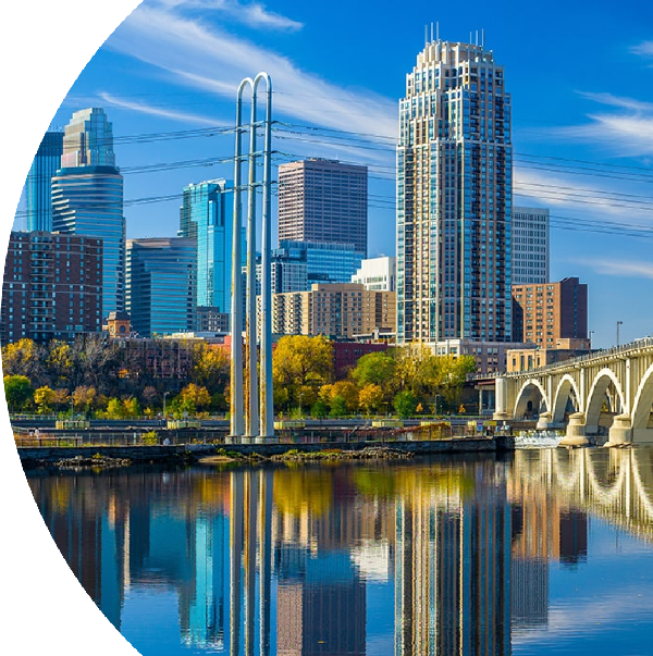 Scenic skyline of Minneapolis, featuring modern skyscrapers and a bridge reflected in the river.