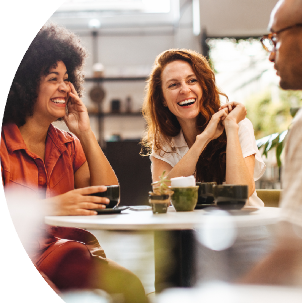 Three people are sitting at a table, smiling and enjoying a conversation over drinks in a relaxed, casual setting