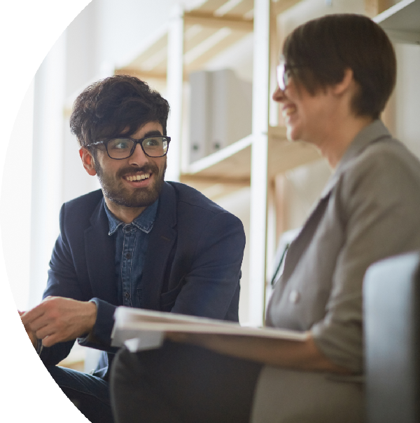 Two people sitting and discussing something, one holding papers, in a professional setting.