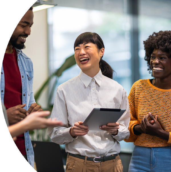 Three people standing and laughing together, one holding a tablet, in a casual conversation.
