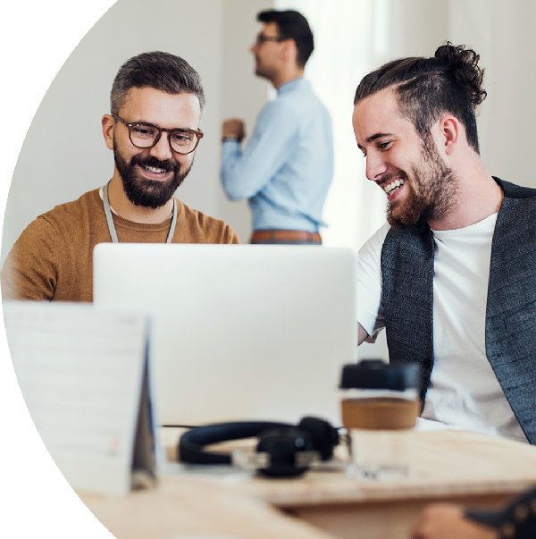 Two people are sitting at a table, smiling and working together on a laptop in a collaborative and casual setting.