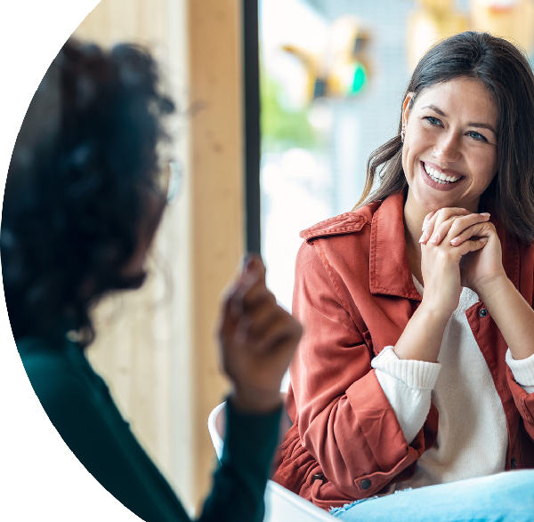 A person is sitting and smiling during a conversation, appearing engaged and relaxed in a casual, friendly setting.