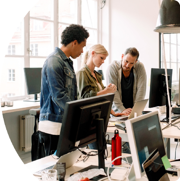 Three people collaborating at a table, looking at a laptop.